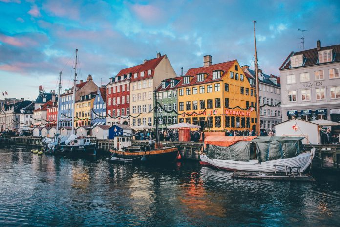 Fotografia da cidade de Copenhage, na qual é possível ver três barcos parados próximos a casas coloridas.