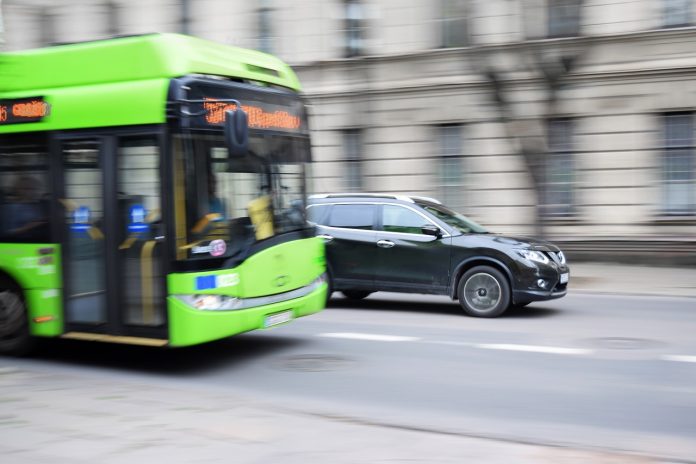 Fotografia de onibus elétrico em movimento na avenida e carro também