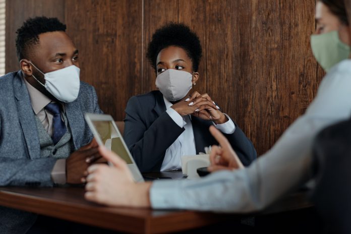 Fotografia de três pessoas em uma reunião utilizando máscaras de prevenção contra o coronavírus.