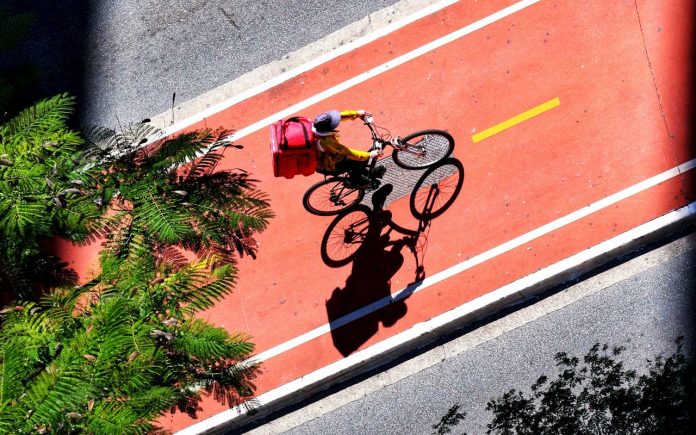 Fotografia de entregador de aplicativo em ciclovia de são paulo como referência no aumento do comércio eleetrônico e delivery nas cidades