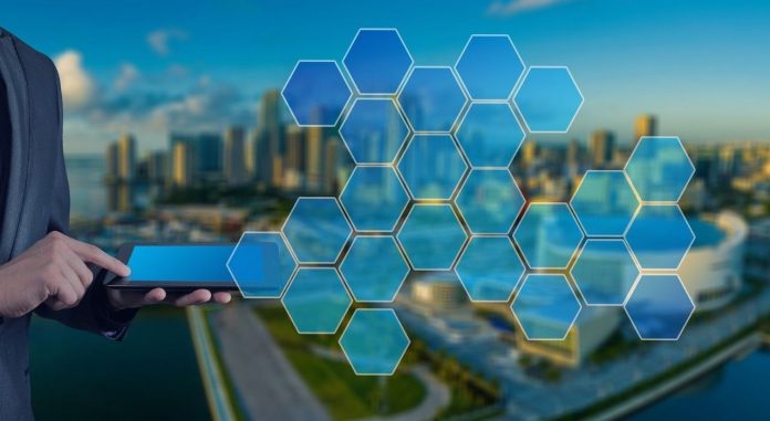 Fotografia e smart cities com representação de homem utilizando tablet e fazendo conexão das tecnologias com a cidade, que está em segundo plano