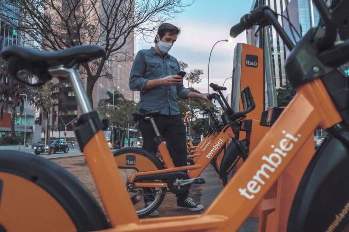 Fotografica de homem jovem usando a tecnologia do celular em bicicletas compartilhadas